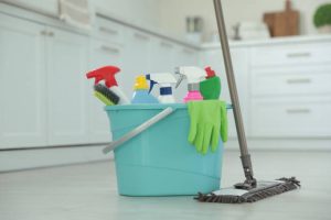 Mop and plastic bucket with different cleaning supplies in kitchen